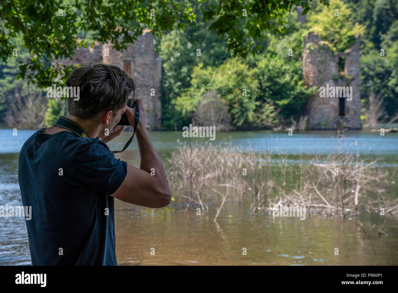 Hombre con una cámara réflex digital de Nikon dispara el ahogado ruinas de castillo del siglo XV Grandval, en Occitanie, Francia. Foto de stock