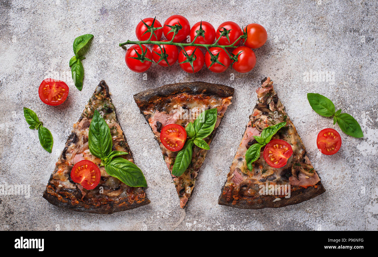 Trozos de pizza negro con tomate y albahaca Foto de stock