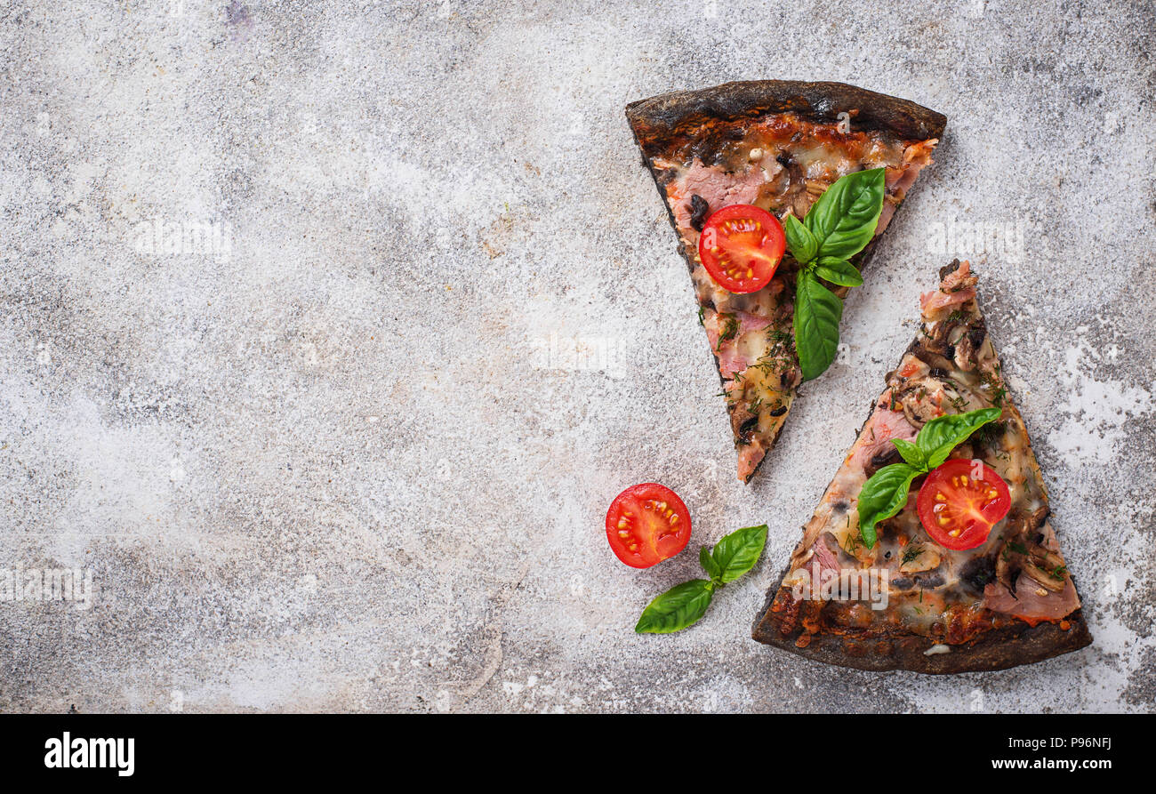 Trozos de pizza negro con tomate y albahaca Foto de stock