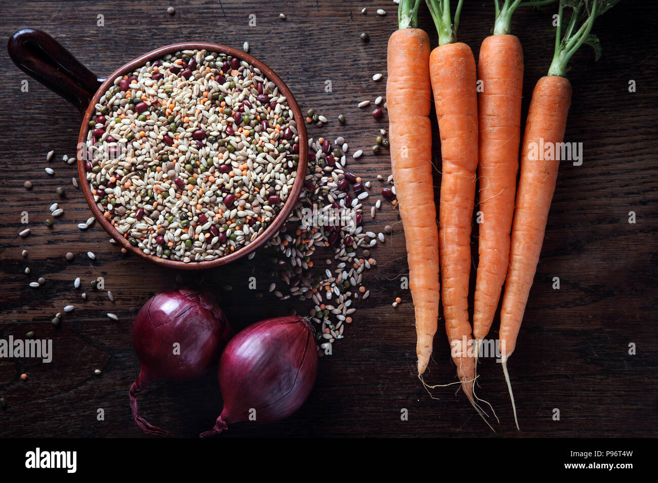 Recipiente de barro con verduras crudas, zanahorias cebollas sobre fondo de madera. Foto de stock