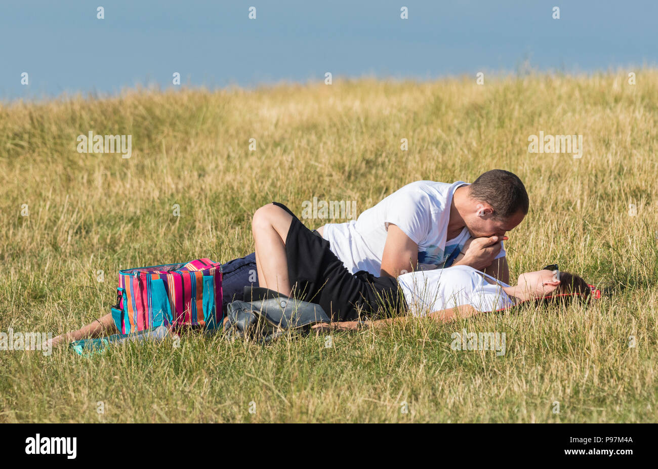 Hombre y mujer joven sentar juntos en un campo en una cálida noche de verano compartiendo un momento de intimidad. Pareja joven en el Reino Unido. Nota:no pueden ser una pareja. Foto de stock
