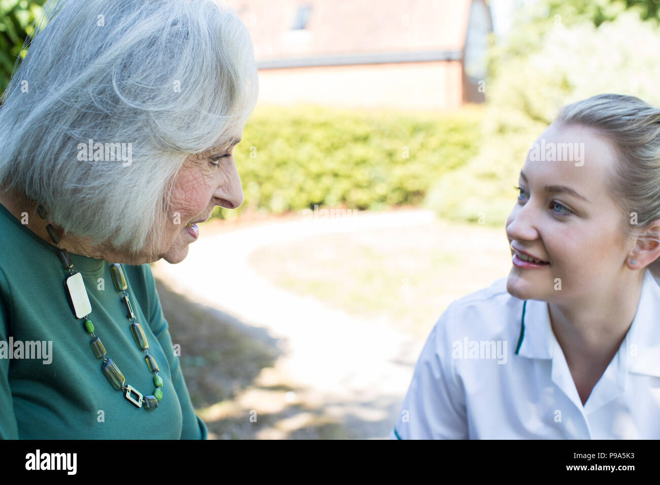 Mujer de más edad en el jardín hablando con cuidador femenino Foto de stock
