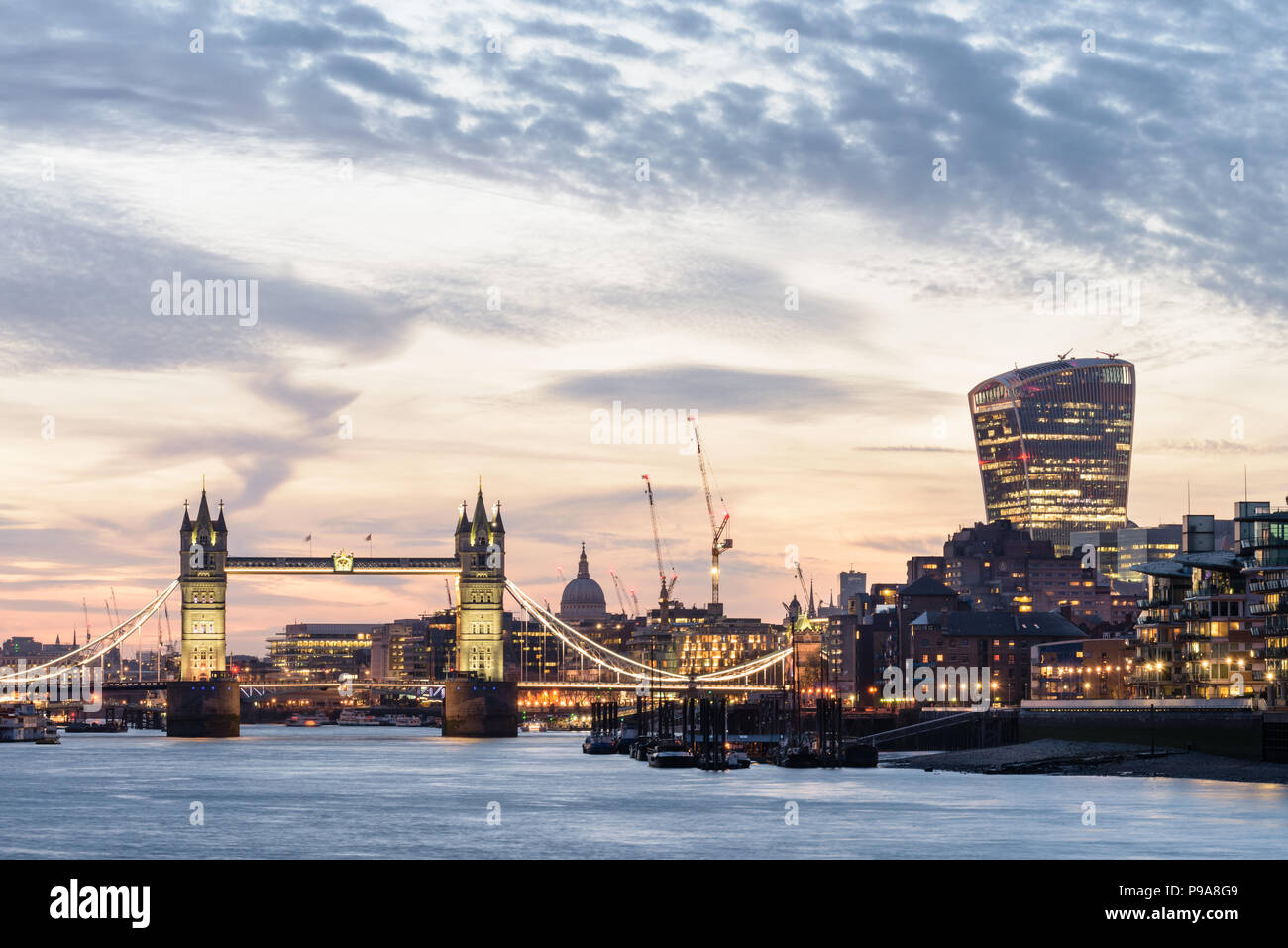 Vista desde el Támesis en Bermondsey, Londres, el Puente de la torre, el walkie talkie y otros edificios riverside iluminado al atardecer con un cielo naranja Foto de stock