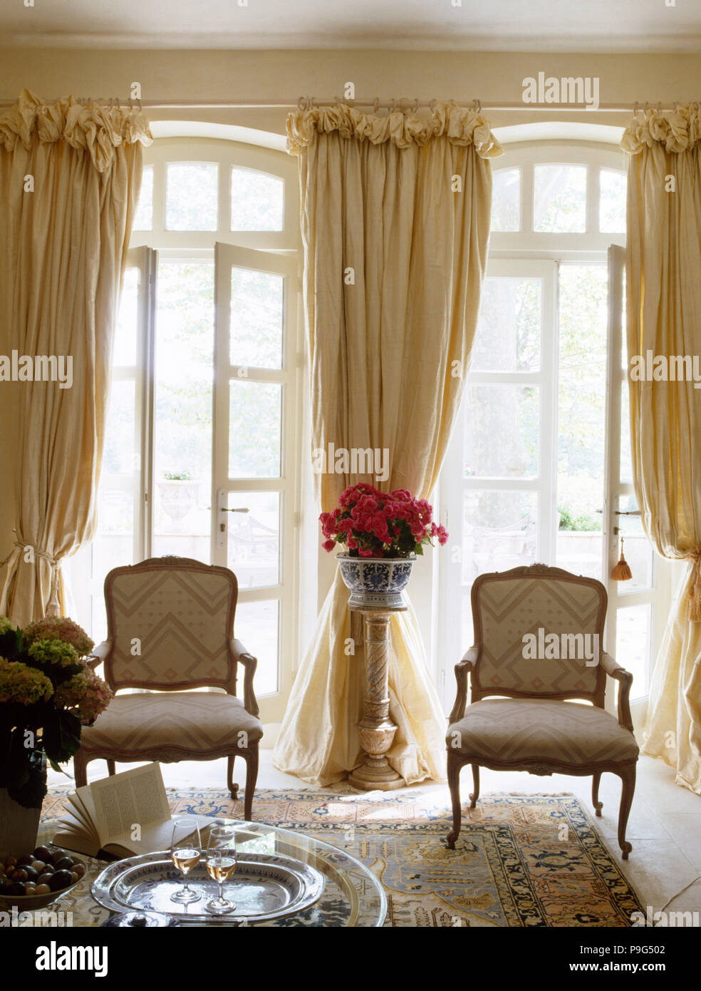 Par de sillas estilo Louis delante de ventanas francesas con pesadas  cortinas color crema en salón provenzal Fotografía de stock - Alamy