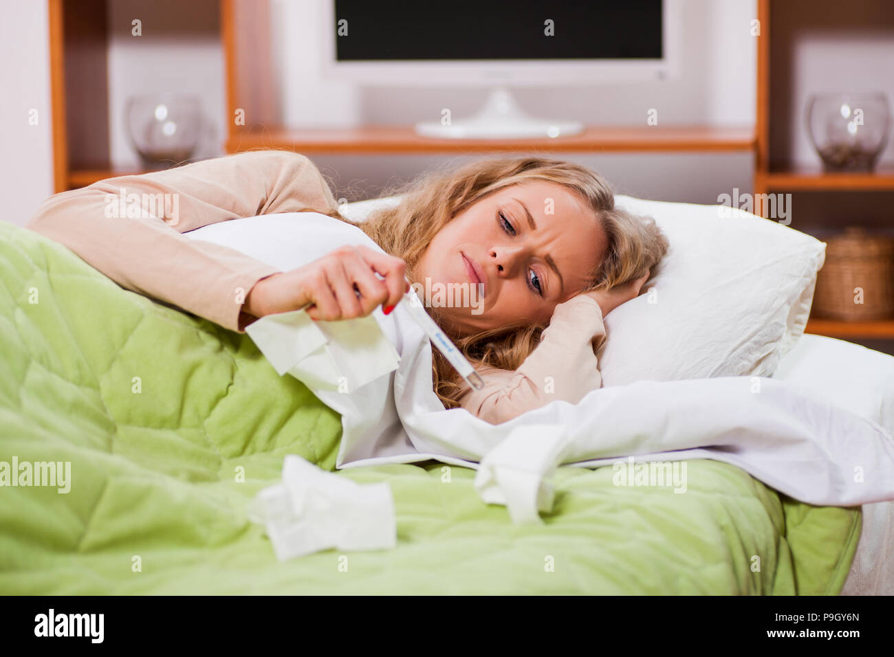 Mujer joven tiene gripe. Ella está acostada en la cama y la medición de la  temperatura corporal Fotografía de stock - Alamy