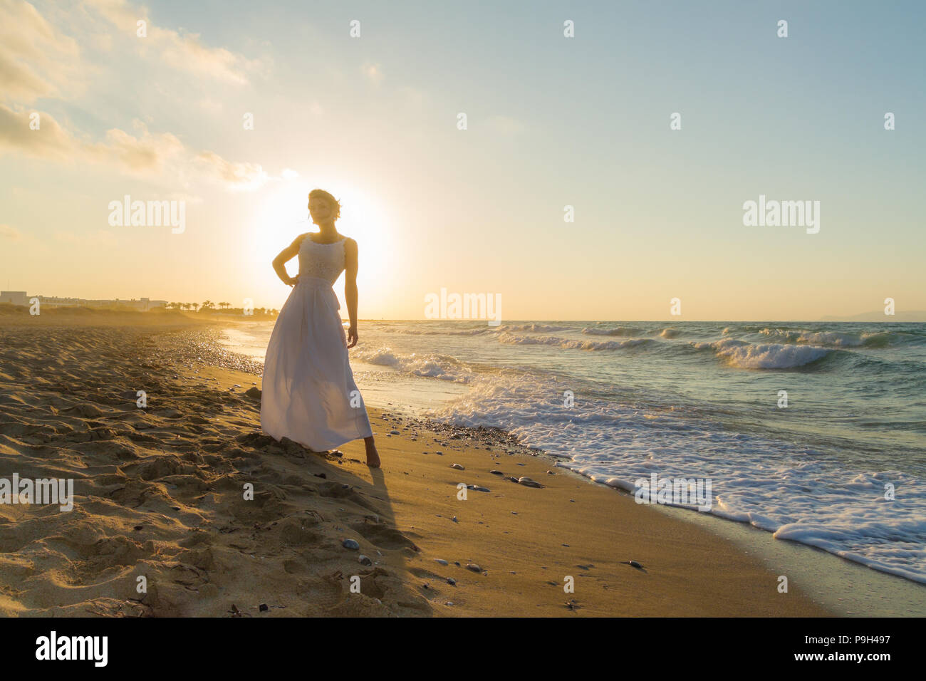 Mujer en vestido blanco, descalzo, sentirse feliz, vivo y libre en la naturaleza meditando en sandy Misty Beach respirar aire fresco del océano limpio al anochecer. Vacaciones de verano concepto de estilo de vida Foto de stock