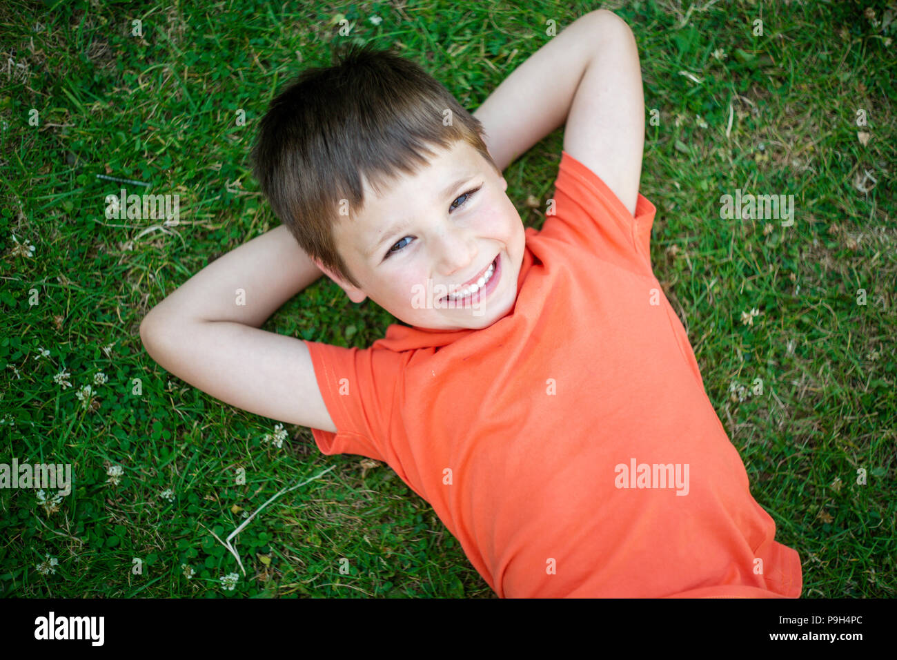 Lindo muchacho feliz 6 años recostados sobre el pasto verde y sonriente. Foto de stock