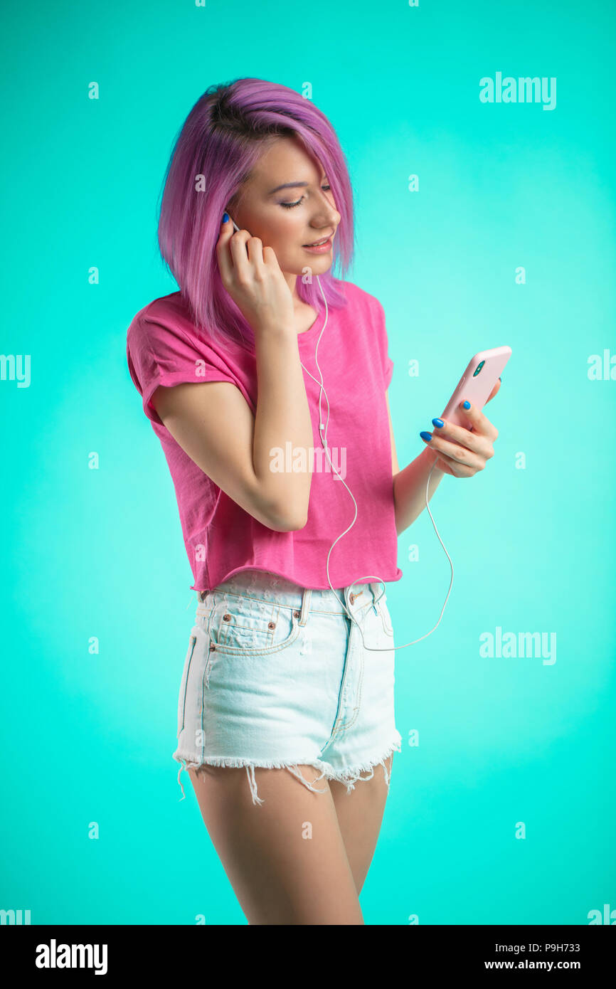Hermosa dama vestida de color rosa en verano casual tela escuchando música  en auriculares. Encantadora chica en pantalones cortos y auriculares  erguido sobre blue back Fotografía de stock - Alamy