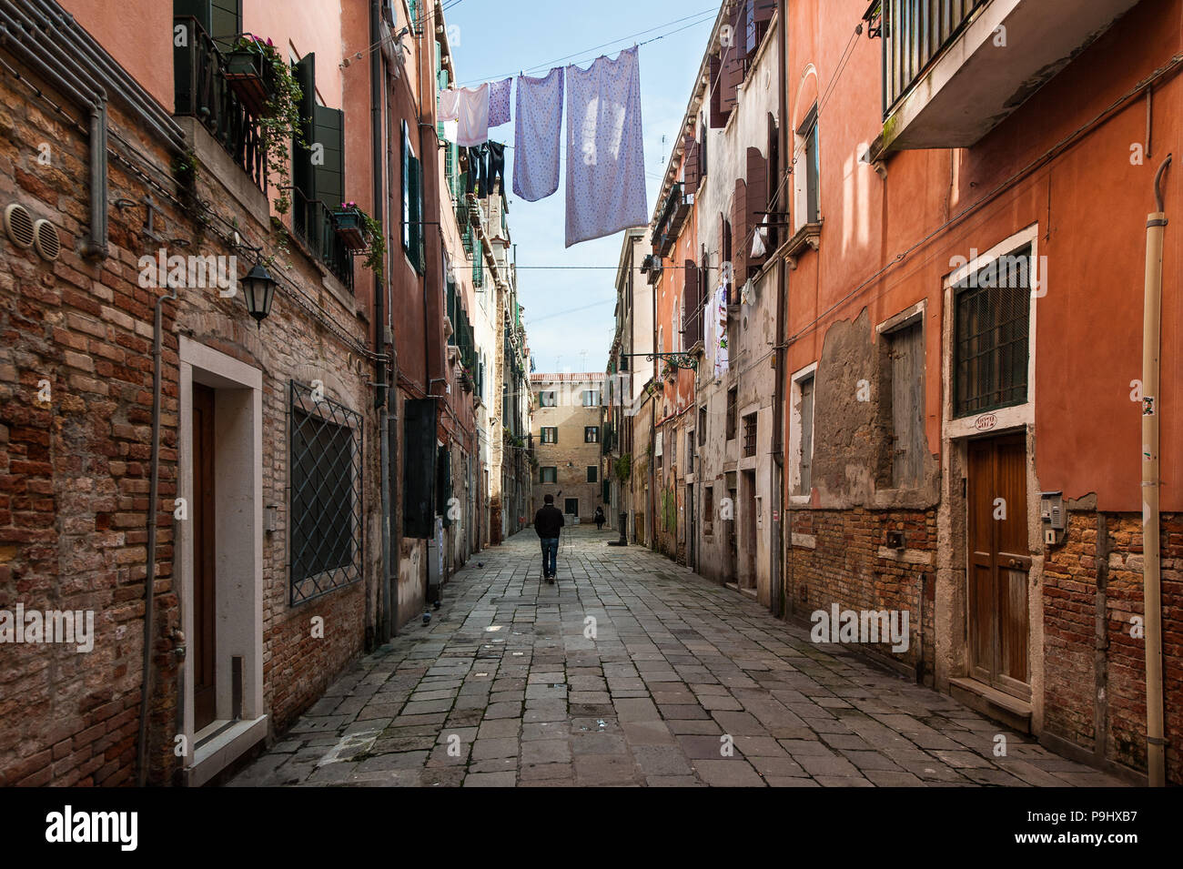 Un hombre que camina sobre una calle casi vacía en el secado de la ropa de cama en Venecia, Italia Foto de stock