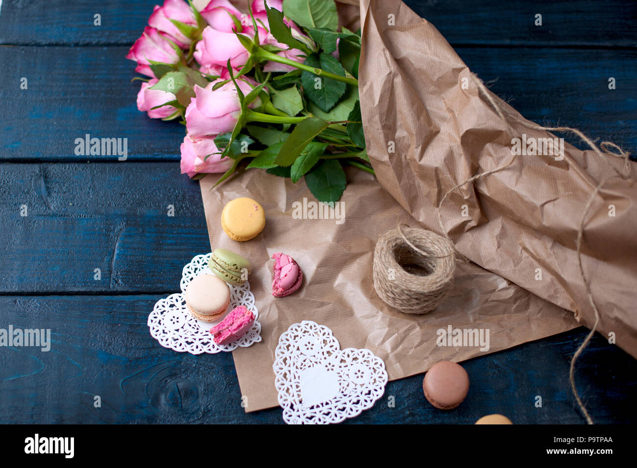 Un ramo de rosas rosa en papel gris y blanco corazones. Pastas dulces  macarons de colores diferentes, el Día de San Valentín. Un lugar gratis  para texto o publicidad Fotografía de stock -