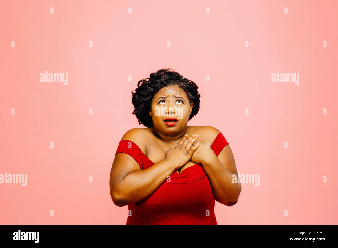 Mujer sosteniendo su pecho y mirando llenos de emoción, aislado sobre fondo de color rosa Foto de stock