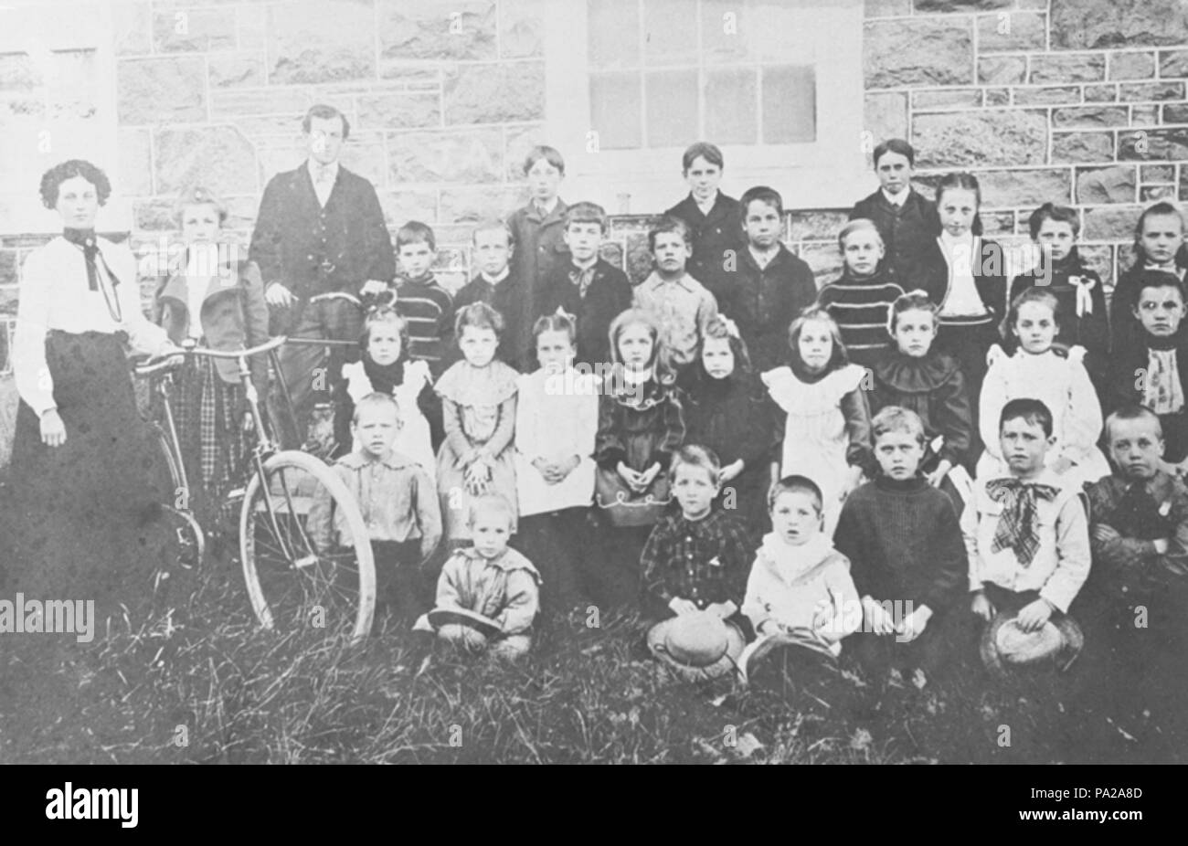 . Inglés: una escuela en blanco y negro fotografía de Whitby, Ontario, Canadá. El Ashburn escuela estaba situada a 780 Myrtle Road West. Fue construido alrededor de 1861 en el lado norte de la novena Concesión de Whitby Township west de Ashburn Road. Fue construido por un albañil de piedra llamado Pearson. Desde 1967, este edificio ha sido utilizado como un centro comunitario. En la fotografía, hay una bicicleta entre Elizabeth Wilson y Laura Holman. El profesor de esta clase es el Sr. McCullough. De izquierda a derecha y de atrás hacia delante: fila posterior: Elizabeth Wilson, Laura Holman, el Sr. McCullough (el maestro), Albert Cook, George DAV Foto de stock