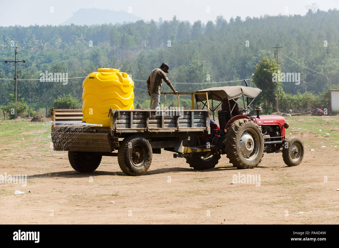 Un agricultor regar un pedazo de tierra seca con un tanque montado en el remolque de un tractor en algún lugar de Karnataka, India. Foto de stock