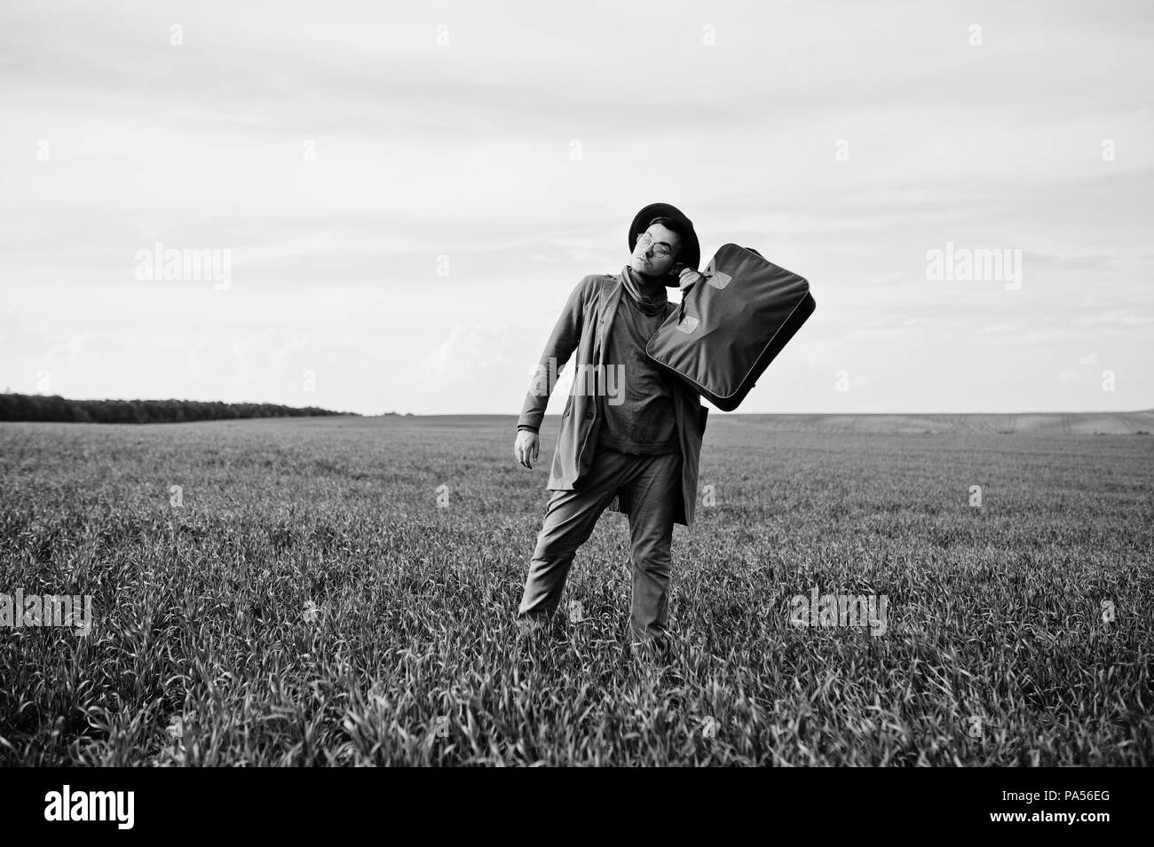 En vidrios, hombre elegante chaqueta marrón y sombrero con bolsa plantean sobre campo verde. Foto de stock