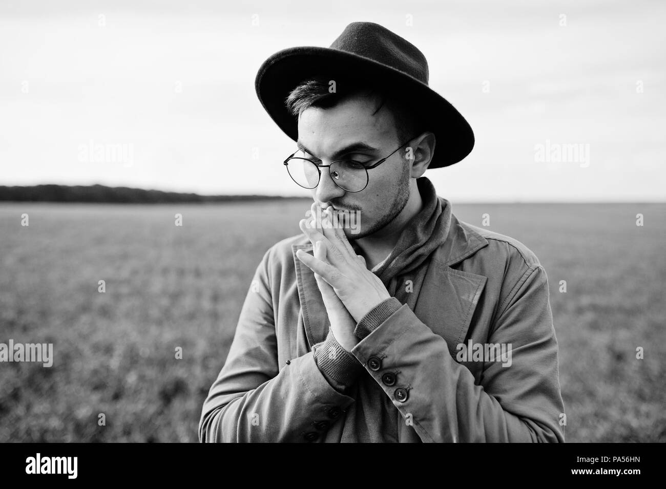 En vidrios, hombre elegante chaqueta marrón y sombrero plantean sobre campo verde. Foto de stock