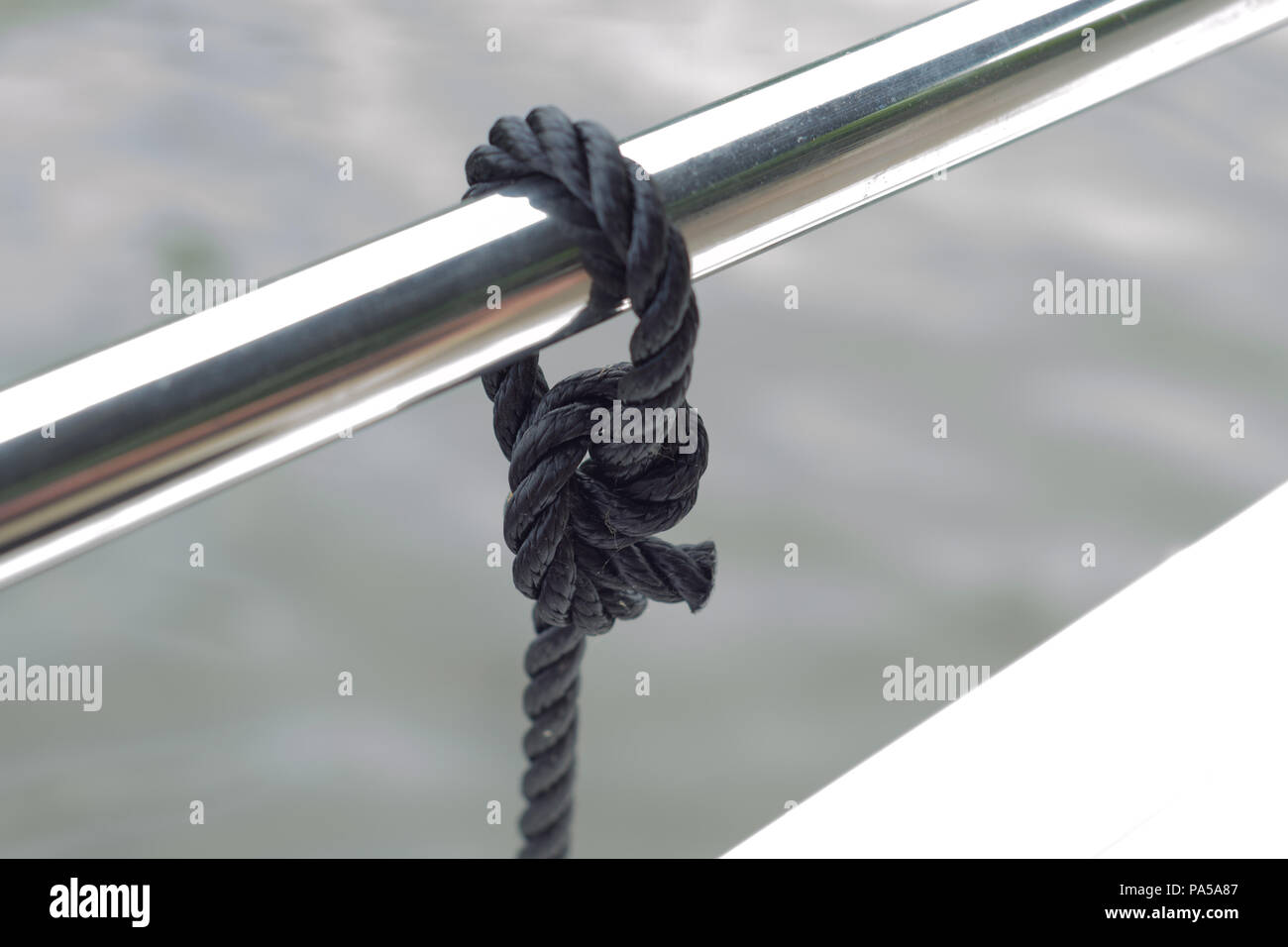 Una cuerda negra atada con un nudo alrededor de una rampa de metal brillante Foto de stock
