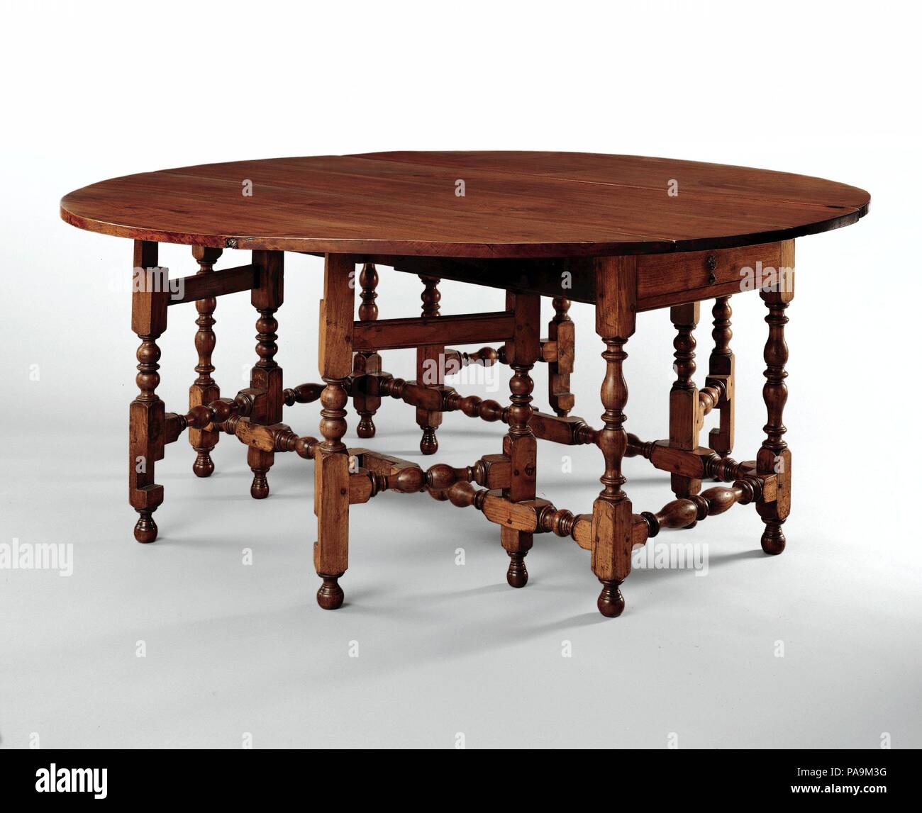 Mesa ovalada con la caída de las hojas. Cultura: American. Dimensiones: 29 3/4 x 74 1/2 x 71. (75.6 x 189.2 x 180.3 cm). Fecha: 1690-1720. Esta espectacular mesa de nogal es tan fina como cualquier hecho en la América colonial. Sus múltiples gira las piernas y gate-like admite crear un bosque virtual de baluster torneados. En contraste con la rectilinearity de tablas del siglo XVII, la suave curva elíptica de su parte superior invita a la convivencia y la conversación entre aquellos sentados alrededor de él. El ancho estrecho de cuero y sillas de caña de este periodo eran ideales para el uso entre los múltiples patas en tablas como tes. Foto de stock