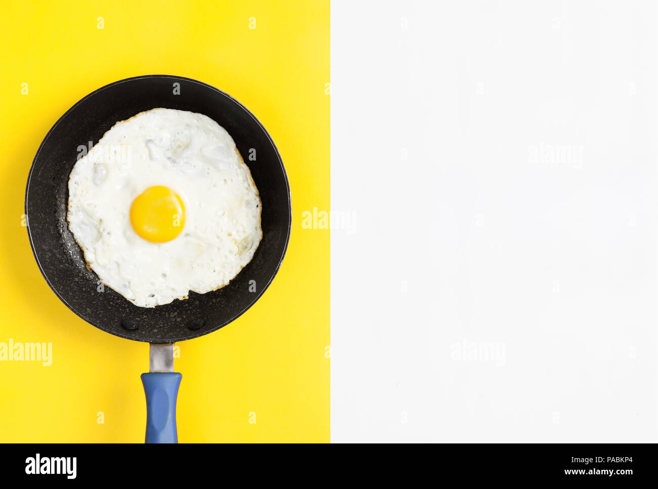 Huevo cocido fresco en una sartén sobre la división del color amarillo y fondo blanco, laicos imagen plana. Foto de stock
