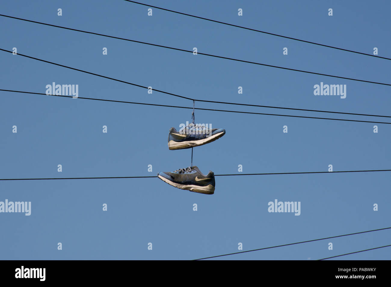 Par de instructores azul o zapatillas colgando de cables telegráficos contra un cielo azul Foto de stock