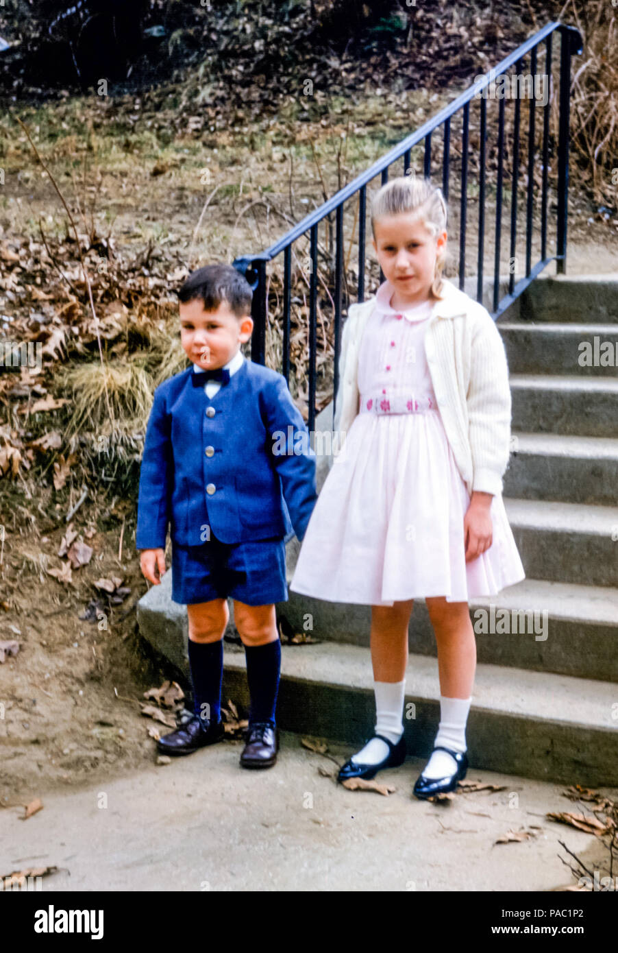 Los niños pequeños aire libre por pasos sosteniendo las manos usando ropa de domingo en EE.UU. En la década 1960. La niña de 5 lleva un vestido fiesta
