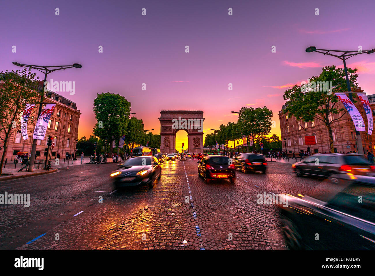 París, Francia - Julio 2, 2017: Avenue des Champs Elysées y el Arc de Triomphe icónica en penumbra con traffic street. Arco del Triunfo en un colorido atardecer cielo. Foto de stock