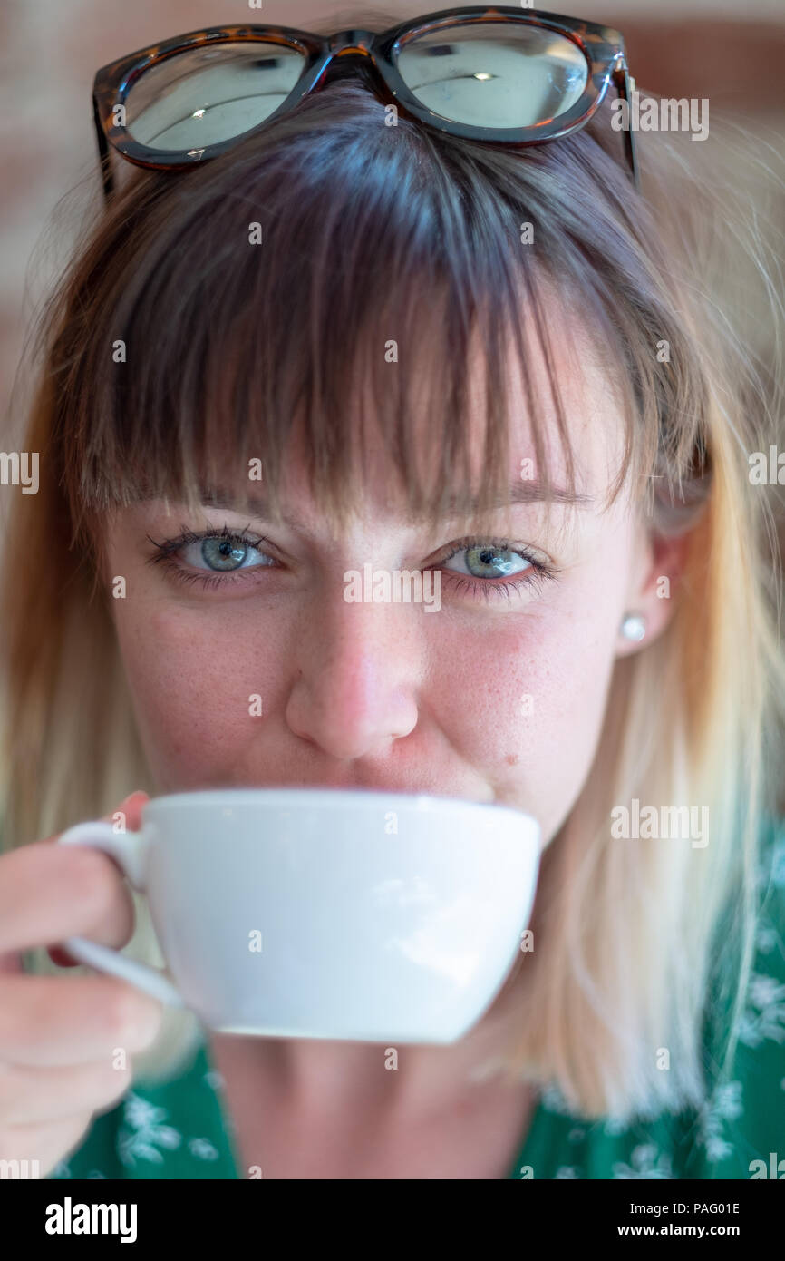 Una joven mujer bebe un café en un café mirando a la cámara. Foto de stock