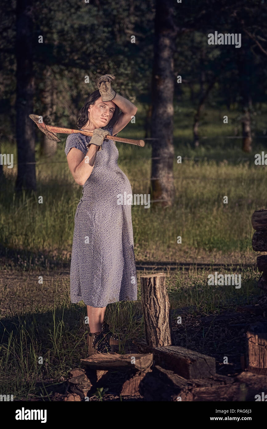 La mujer embarazada que llevaba un vestido y botas cortando madera en un  rancho en una zona rural del norte de California Fotografía de stock - Alamy
