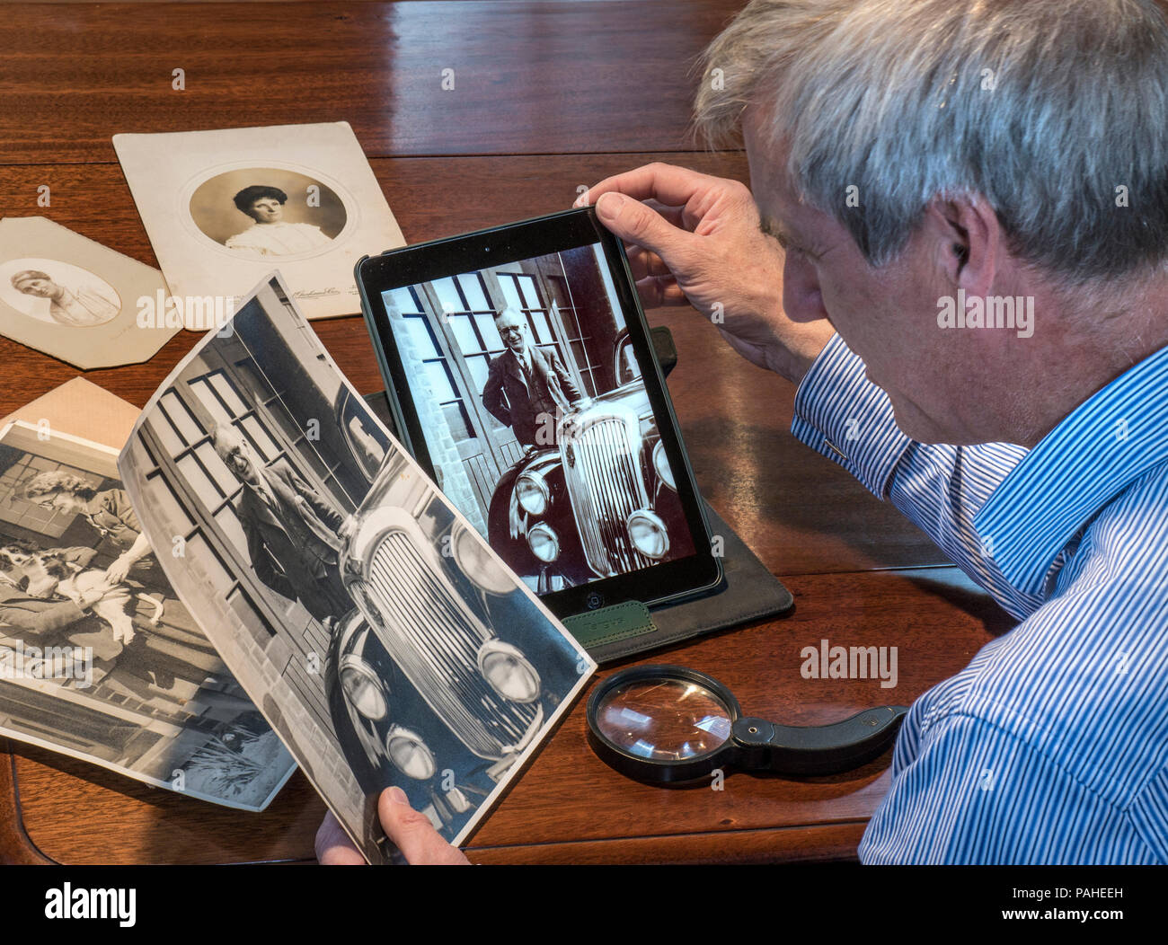 Hombre maduro ordenar a través de viejas fotografías compara un original B&W imprimir con la imagen escaneada en su tablet pc Foto de stock