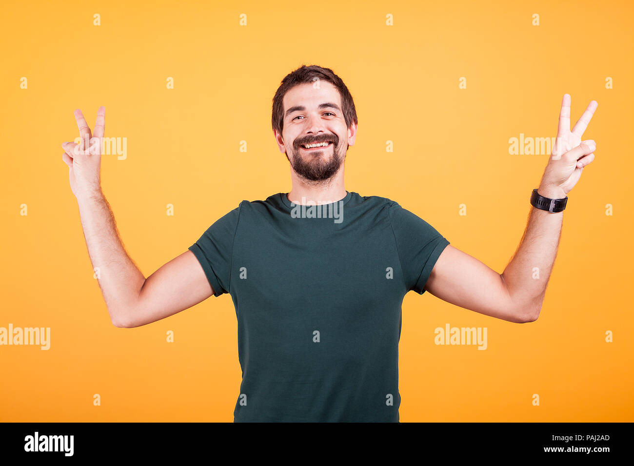 Feliz el hombre sonriente mostrando victoria signo de paz con ambas manos isoalted sobre fondo amarillo en studio Foto de stock