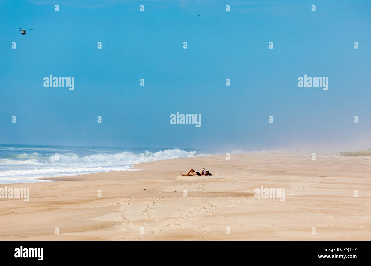 Sola mujer recostada sobre una toalla en la playa con un heilcopter volando en Amagansett, NY Foto de stock