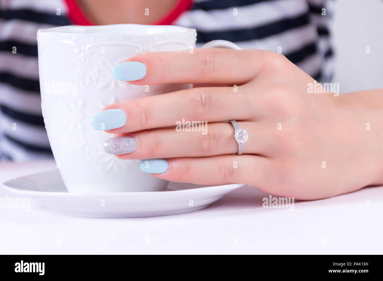Chica mano con azul Manicura Uñas polaco y diamantes anillo de compromiso  sosteniendo una taza de café en sailor t-shirt en segundo plano. Y las  vacaciones de verano Fotografía de stock -