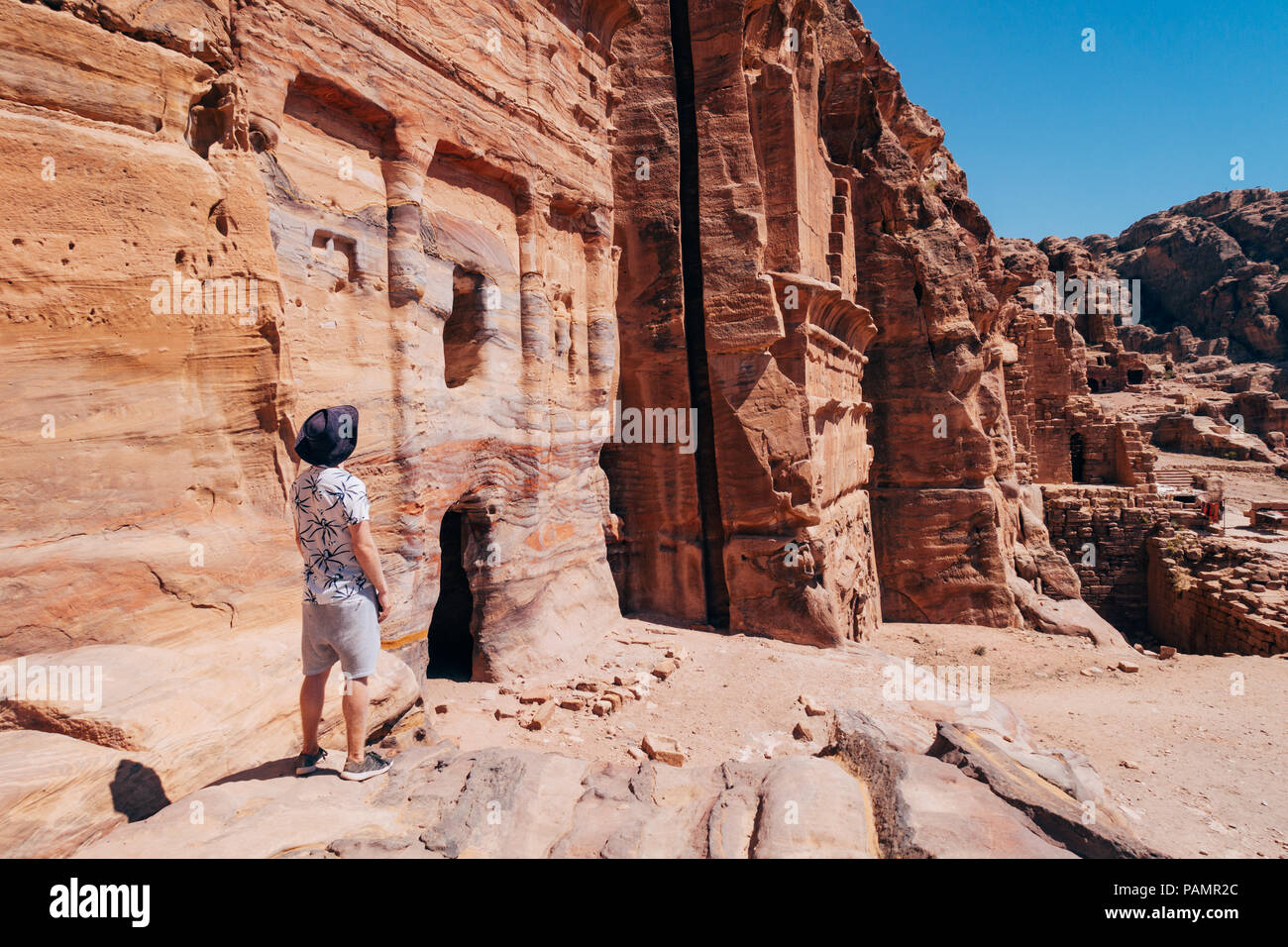 Un turista plantea en una repisa de roca mirando por encima de una tumba en la entrada de la ciudad perdida de Petra, Jordania Foto de stock
