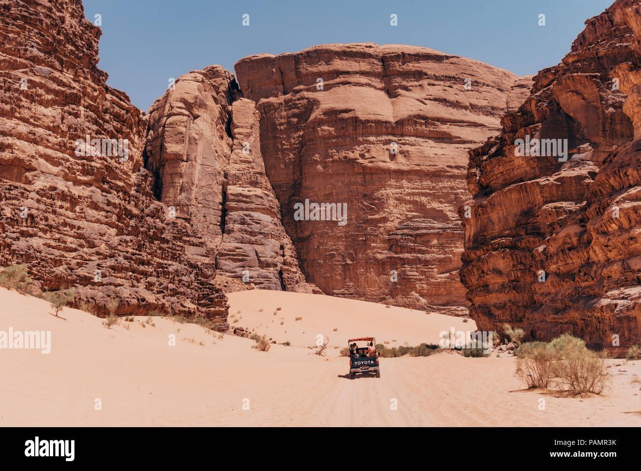Una camioneta Toyota es eclipsado como unidades entre las enormes formaciones rocosas del Parque Nacional en Wadi Rum, Jordania Foto de stock