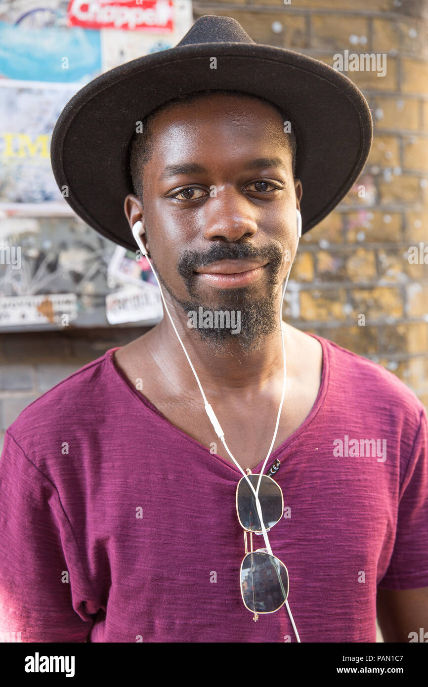 Cool, Hip, hipster, negro hombre que llevaba un sombrero de ala grande y  blanco auriculares delante de una pared de ladrillo en Brick Lane en  Shoreditch, Londres, Reino Unido Fotografía de stock -