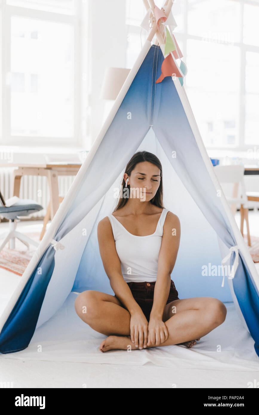 Mujer joven sentado con las piernas cruzadas en una carpa en su casa, con los ojos cerrados Foto de stock