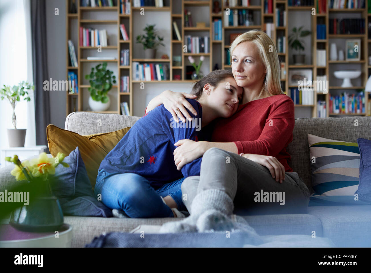 Madre e hija adolescente sentado en el sofá con brazos alrededor Foto de stock