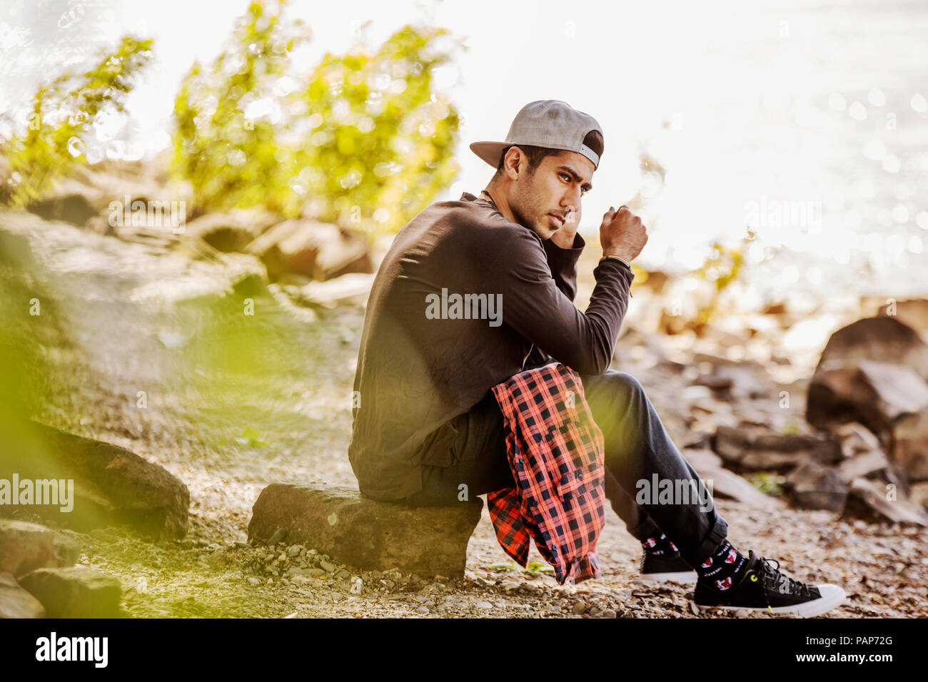 Joven hombre que llevaba una gorra de béisbol sentado en la naturaleza Foto de stock