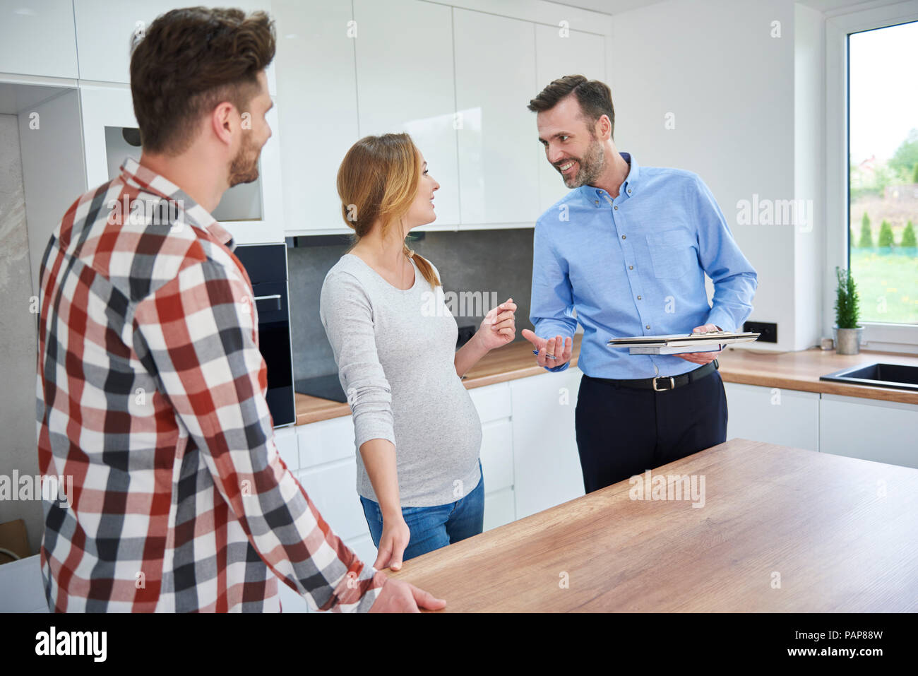 Pareja y agente de la propiedad inmobiliaria hablando en la cocina del apartamento nuevo Foto de stock