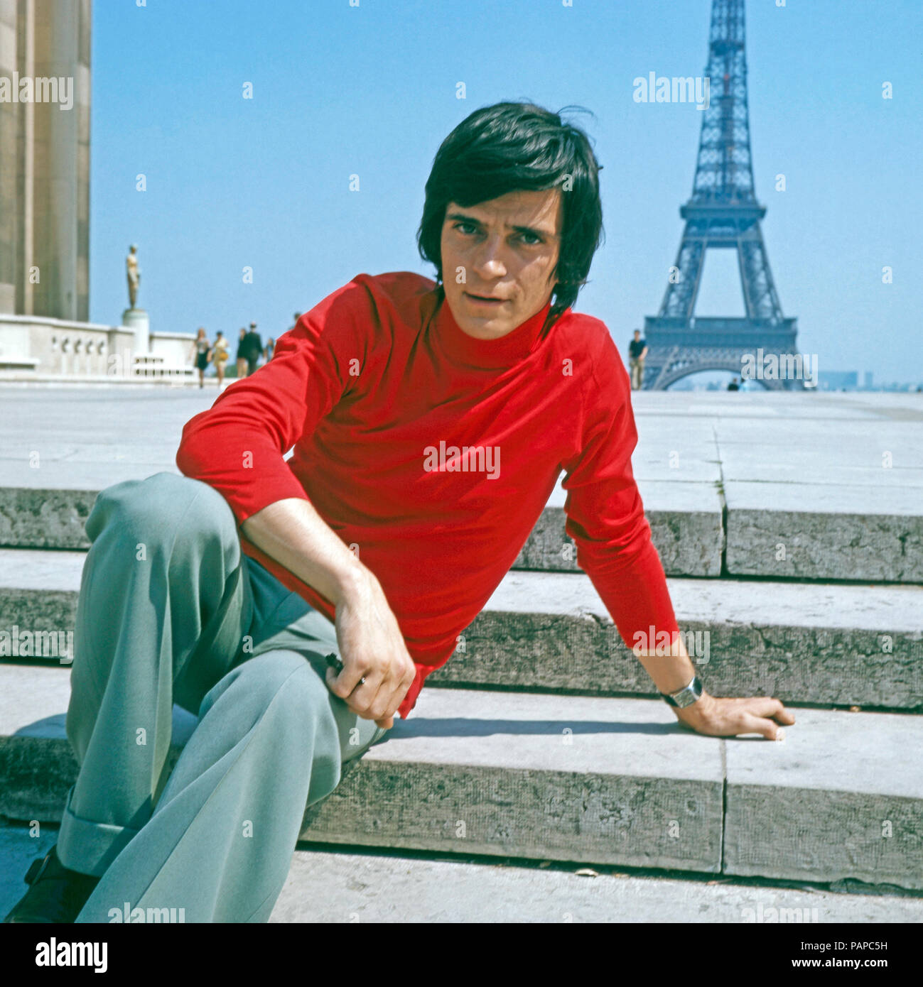 Ein junger Mann en rotem Rollkragenpulli posiert für den Fotografen en  Paris, Frankreich 1970. Un joven hombre que llevaba un suéter de cuello de polo  rojo posando para el fotógrafo en París,
