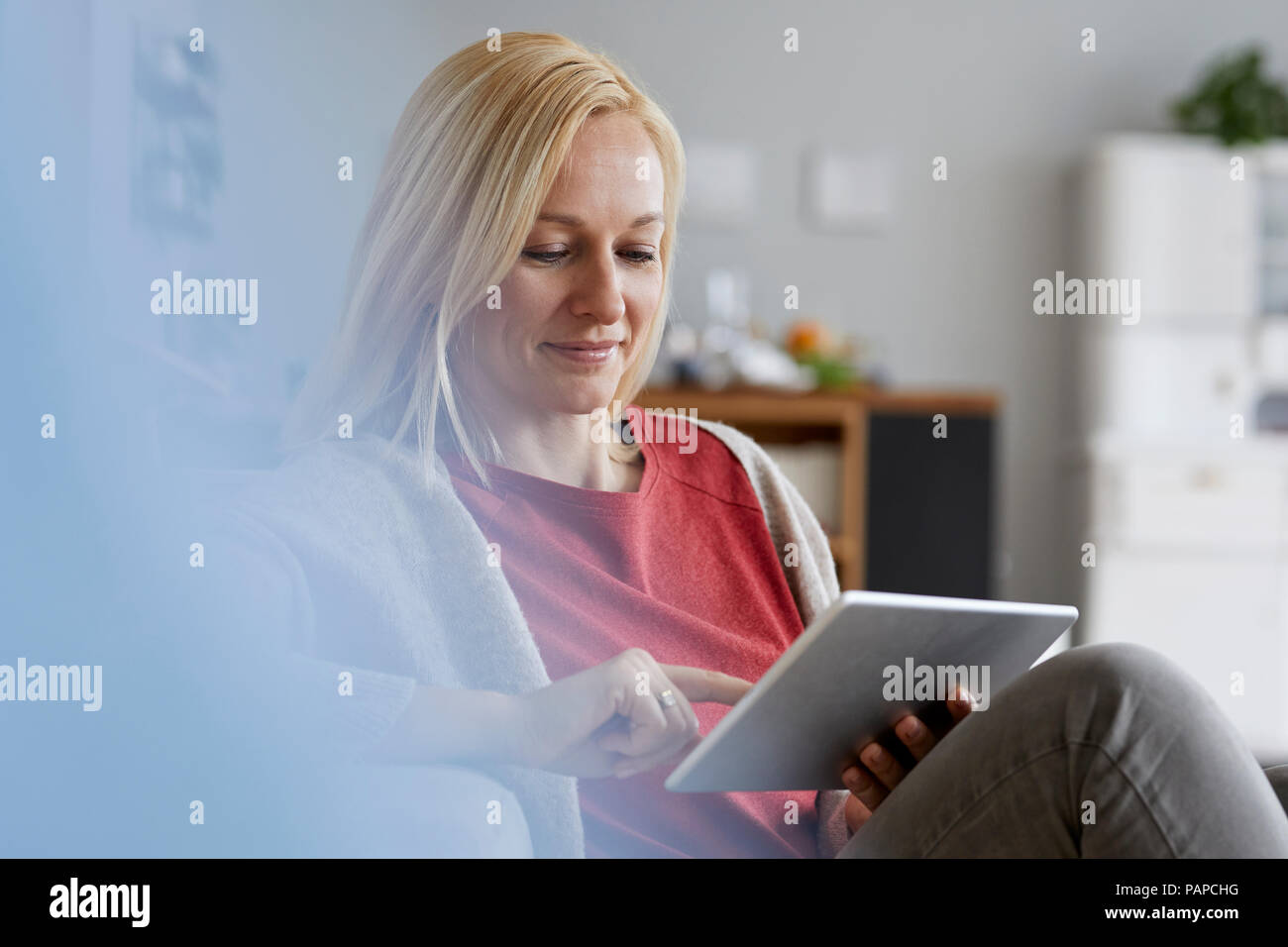 Mujer rubia sentada en su casa, utilizando tablet digital Foto de stock