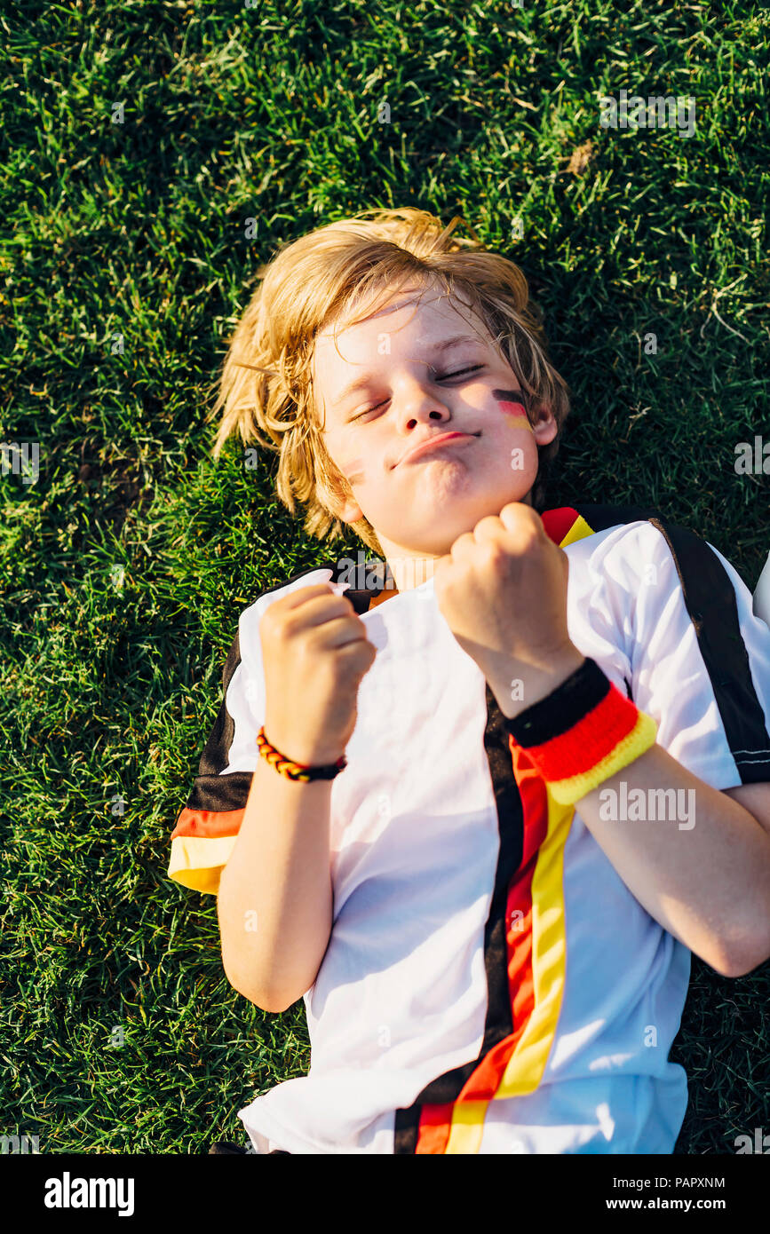 Boy en alemán soccer shirt acostado en el pasto, mantener los dedos cruzados para el mundo chamiponship Foto de stock