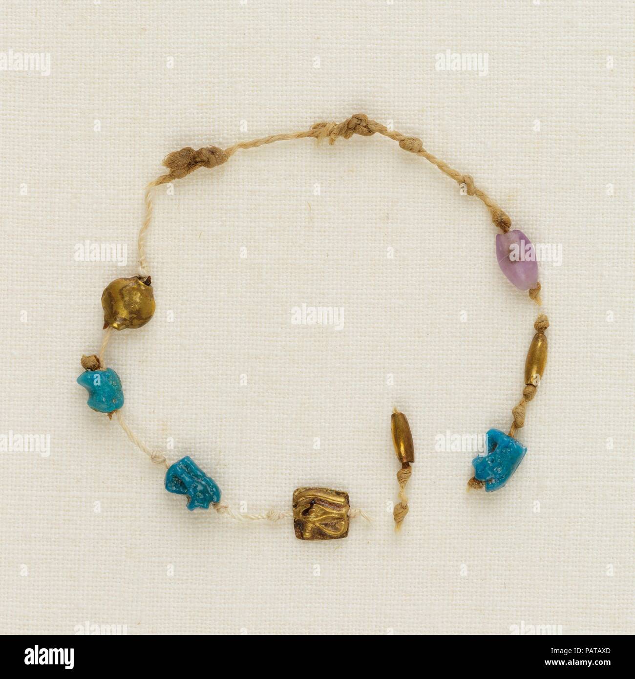 Brazalete con 4 ojos wedjat, 2 cordones de barril y 1 cordón de acacia. Dimensiones: Diam. ca. 3,8 cm (1 1/2"). Dinastía: Dinastía tardía 21. Fecha: ca. 1000-945 A.C. Uno de los cinco brazaletes encontrado alrededor de la muñeca derecha de la momia Henettawy, este es un solo hilo de cordoncillo. Encuerda a intervalos a lo largo del Strand fueron cuatro ojos wedjat amuletos, tres de loza y uno de oro; una de oro y una amatista; y un cordón de barril de oro Cordón de acacia. El cable estaba roto, por lo que el orden original de los abalorios y amuletos es incierto. Los ojos wedjat representan el sanado el ojo del dios halcón Horus, un potente sym Foto de stock