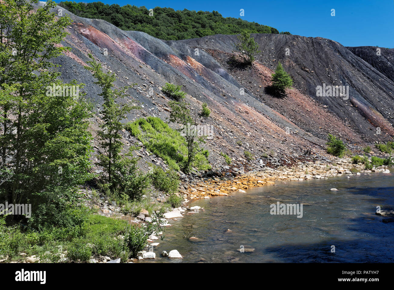Residuos de los relaves de la mina de carbón la pila de escombros, al lado de un arroyo con piedras naranja mostrando los daños ambientales de contaminación tóxica y drenaje ácido de mina. Foto de stock