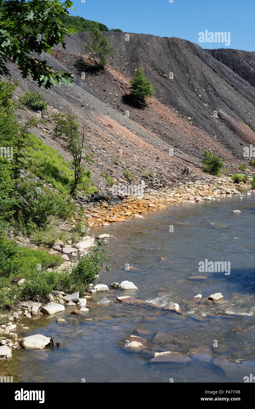 Residuos de los relaves de la mina de carbón la pila de escombros, al lado de un arroyo con piedras naranja mostrando los daños ambientales de contaminación tóxica y drenaje ácido de mina. Foto de stock