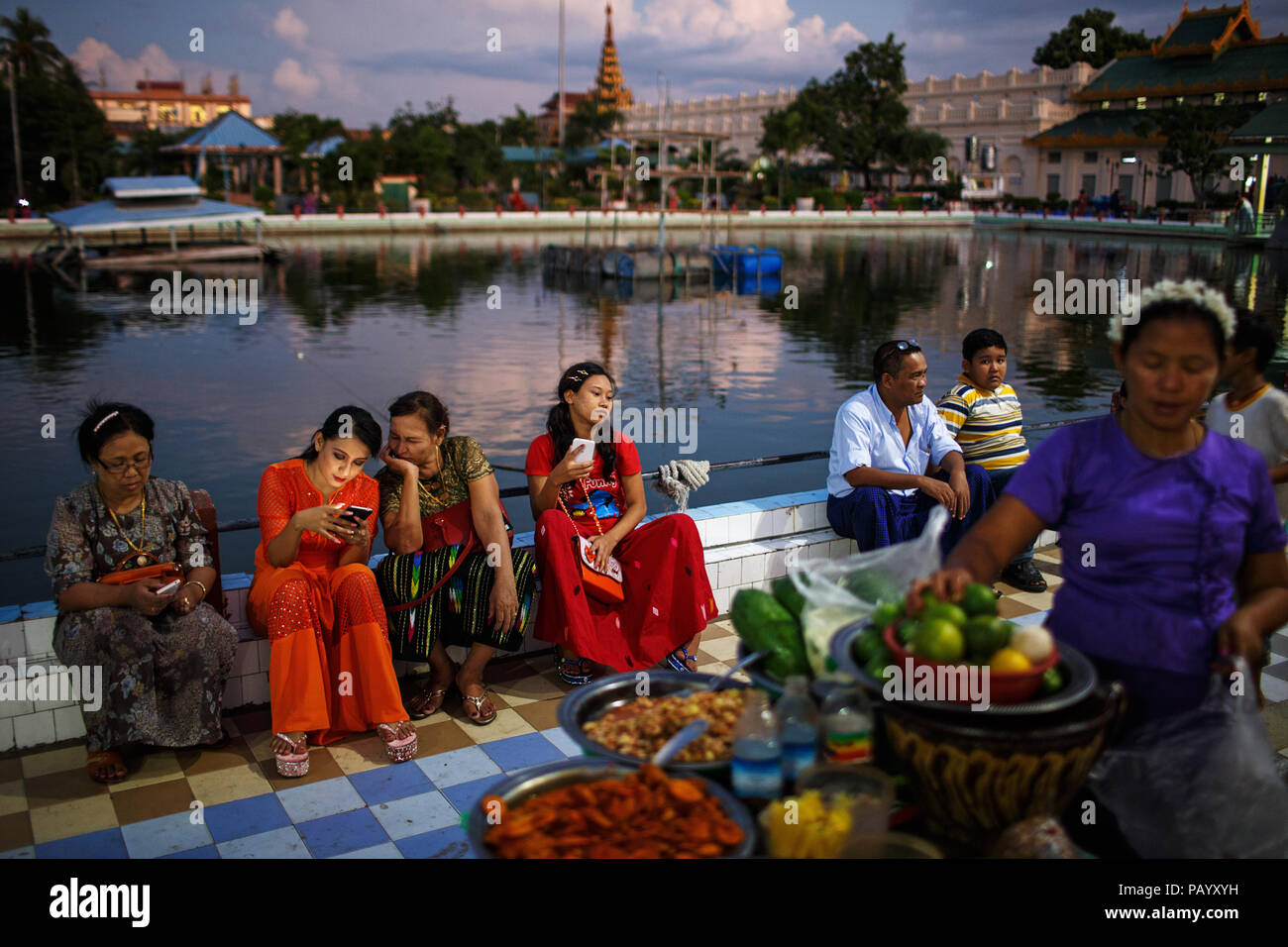 Un grupo de personas disfruta del atardecer en un parque cerca de la Pagoda de Mahamuni, en Mandalay, Myanmar. Foto de stock