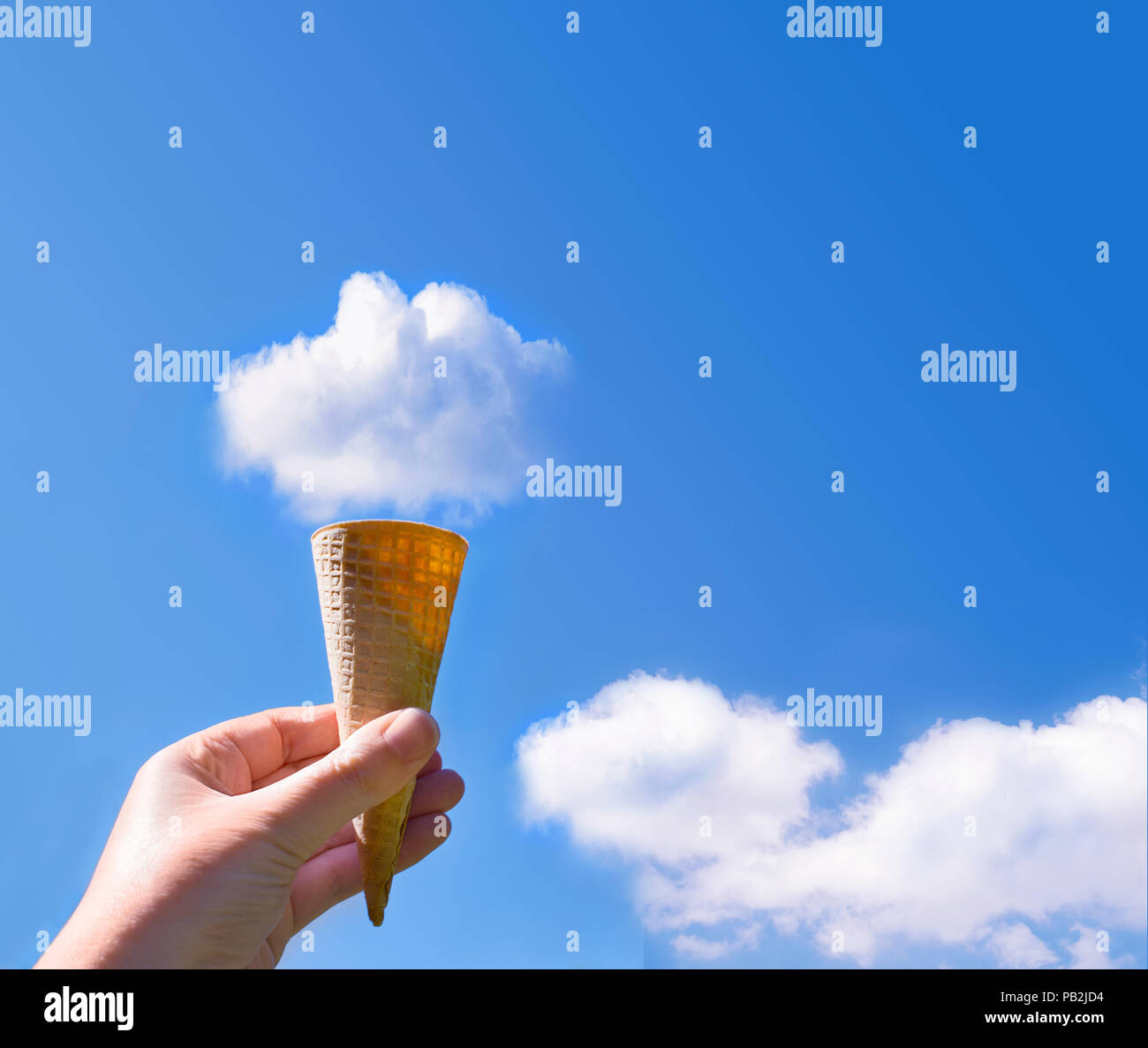 Imagen de la mano que sostiene el cono de helado en el cielo con nubes esponjosas en la parte superior del cono Foto de stock