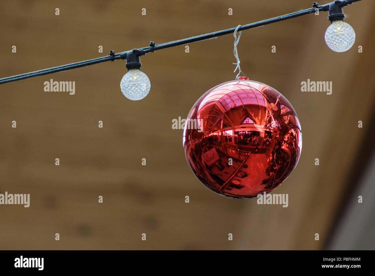 Rojo bola ornamental reflejando el mall flanqueado por globe luces en Navidad. Foto de stock