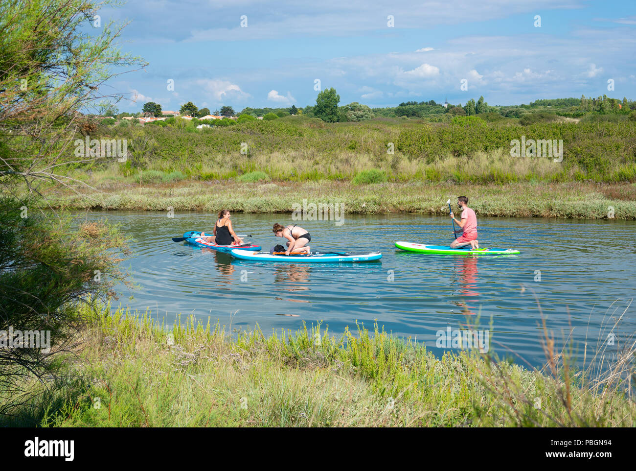 La Vendée, Francia, 23 de julio de 2018: tres jóvenes disfrutan haciendo el Stand Up Paddle en un tranquilo río en verano caluroso día Foto de stock