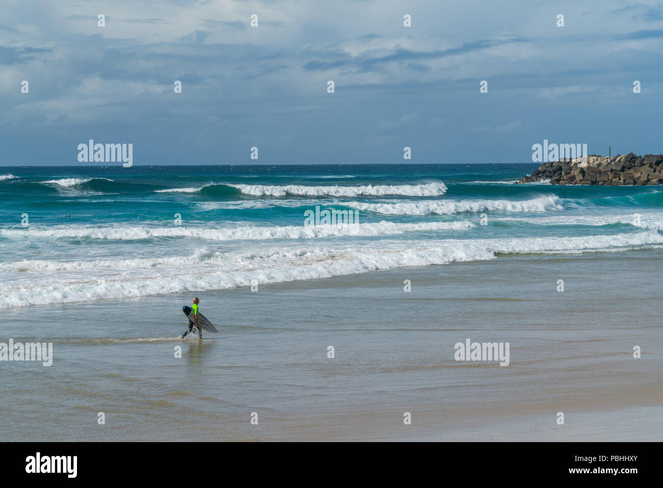 COOLANGATTA, AUSTRALIA - 10 de julio de 2018; la amplia playa de surf con surfer llevar tablas de surf a lo largo de la playa en frente del surf Foto de stock