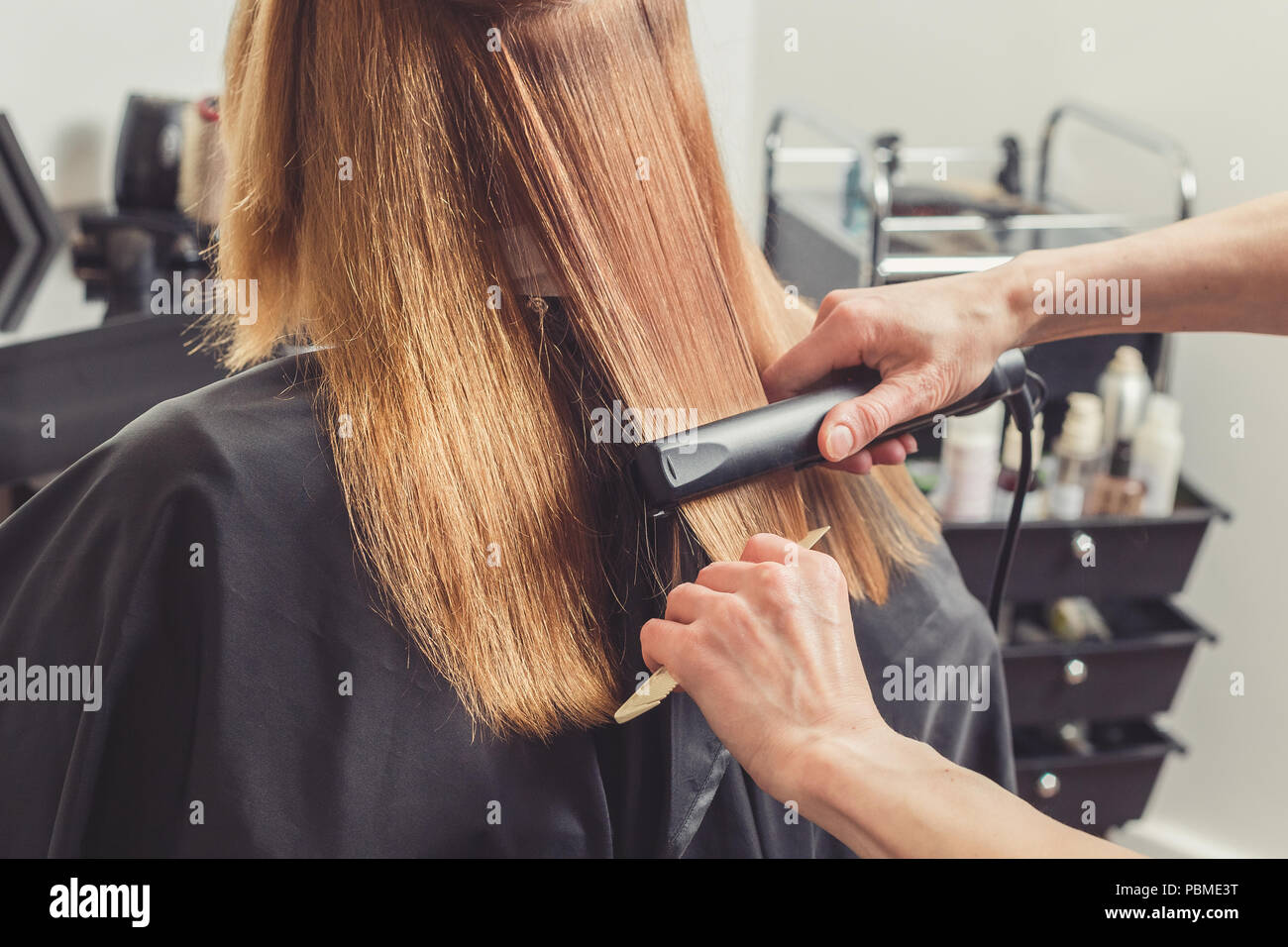 Alisar el cabello en un salón de belleza. Peluquería haciendo un peinado  para un cliente con una plancha de cabello Fotografía de stock - Alamy